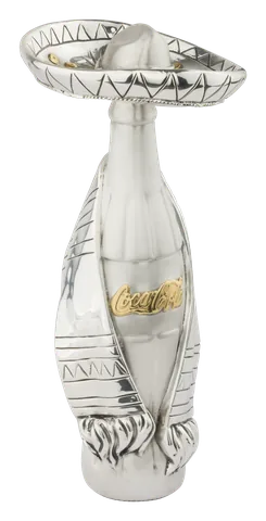 A Coca-Cola bottle wearing a charro hat and sarape, in silver with the Coca-Cola script in gold