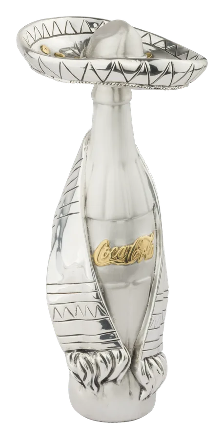 A Coca-Cola bottle wearing a charro hat and sarape, in silver with the Coca-Cola script in gold