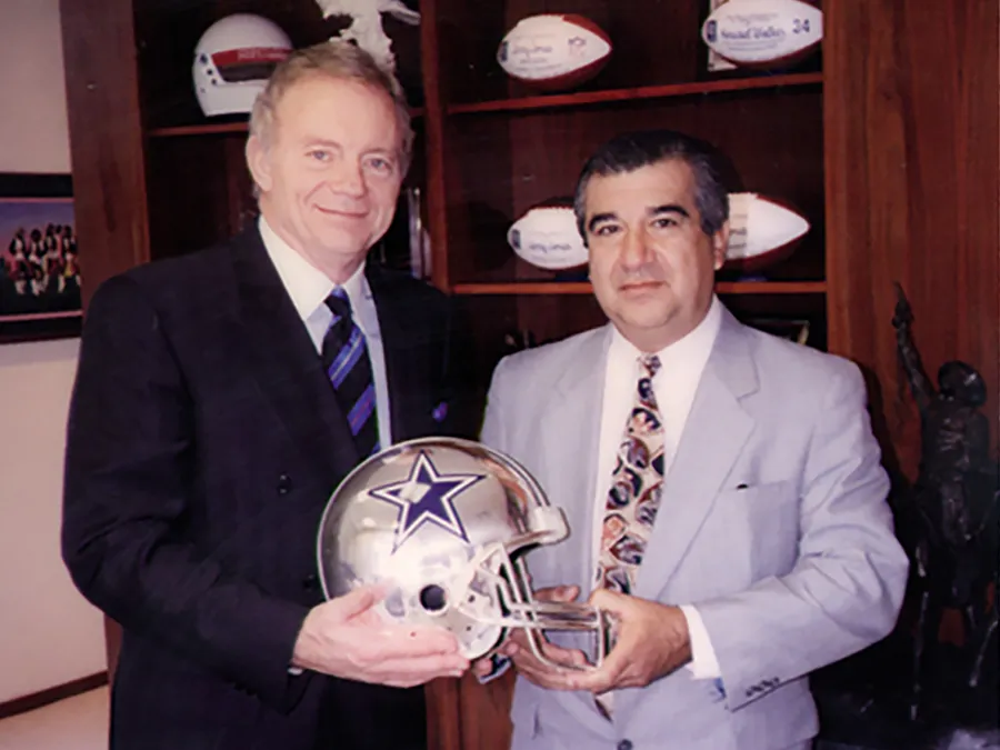 Jerry Jones, הבעלים של ה-Dallas Cowboys, מחזיק קסדת כסף של D’Argenta לצד גבר נוסף במשרד מעוטר בפריטי פוטבול